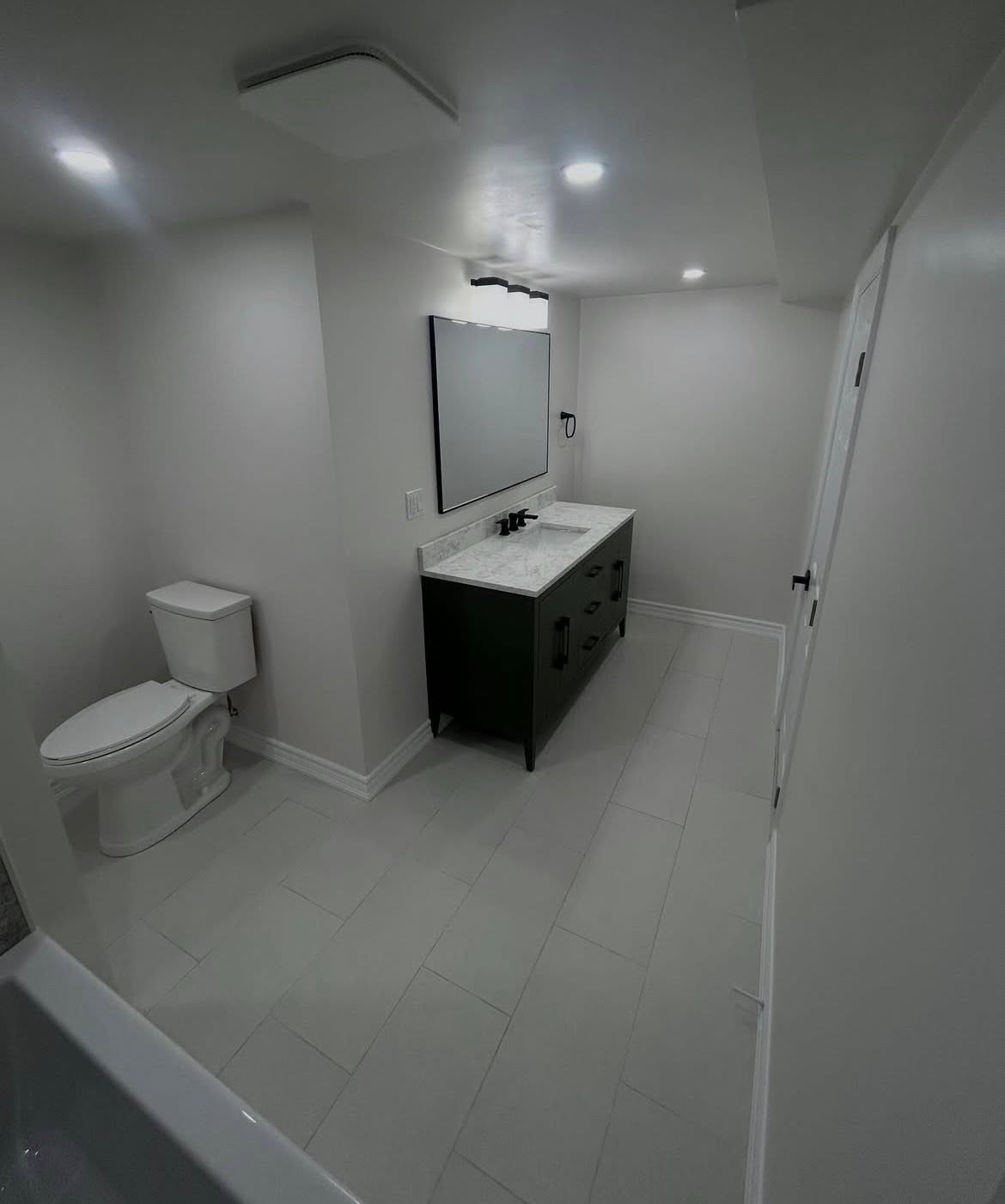 Bathroom with a dark vanity, white fixtures and recessed lighting.
