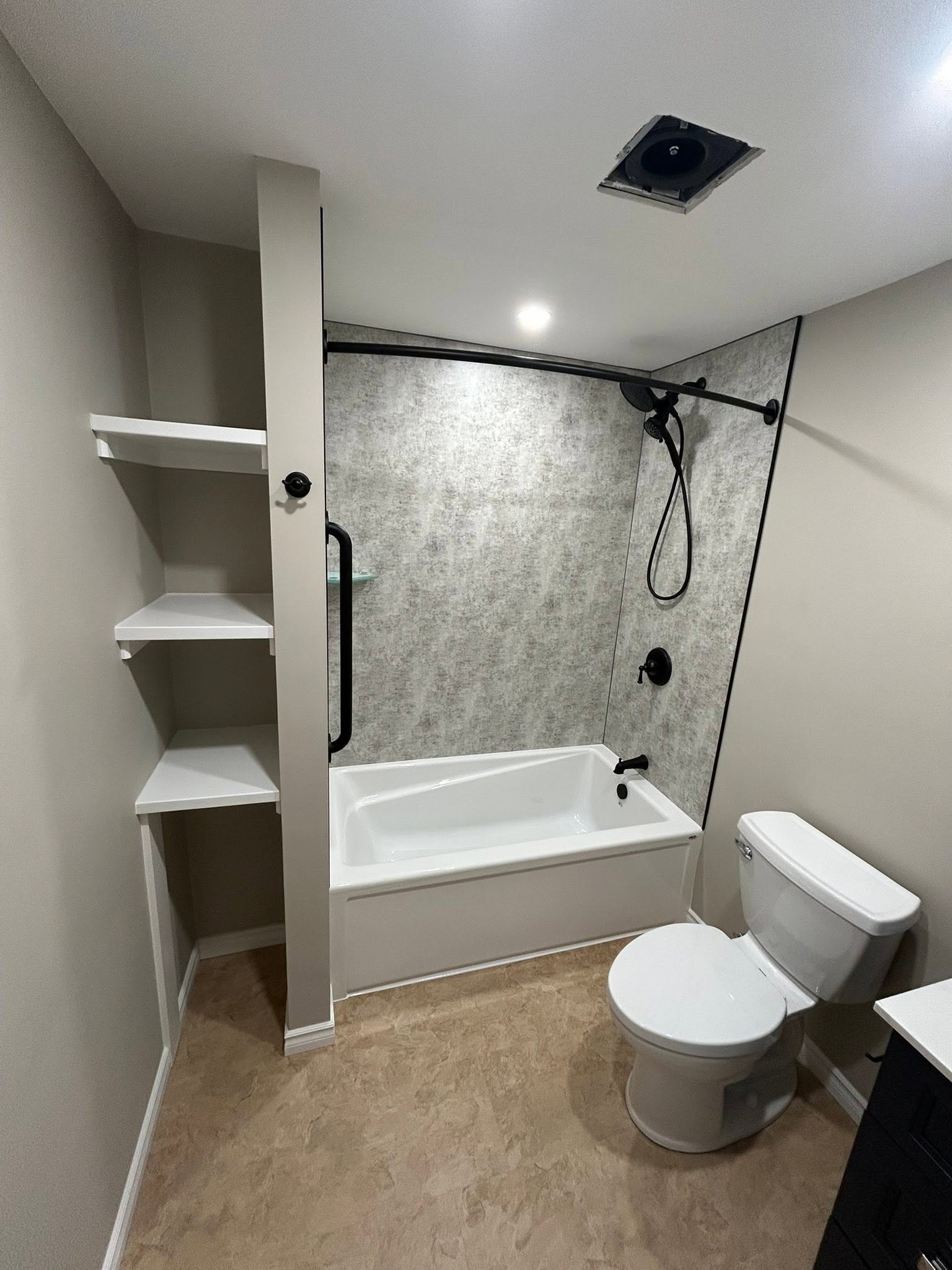 Built-in open shelving beside a bathtub with dark shower fixtures.