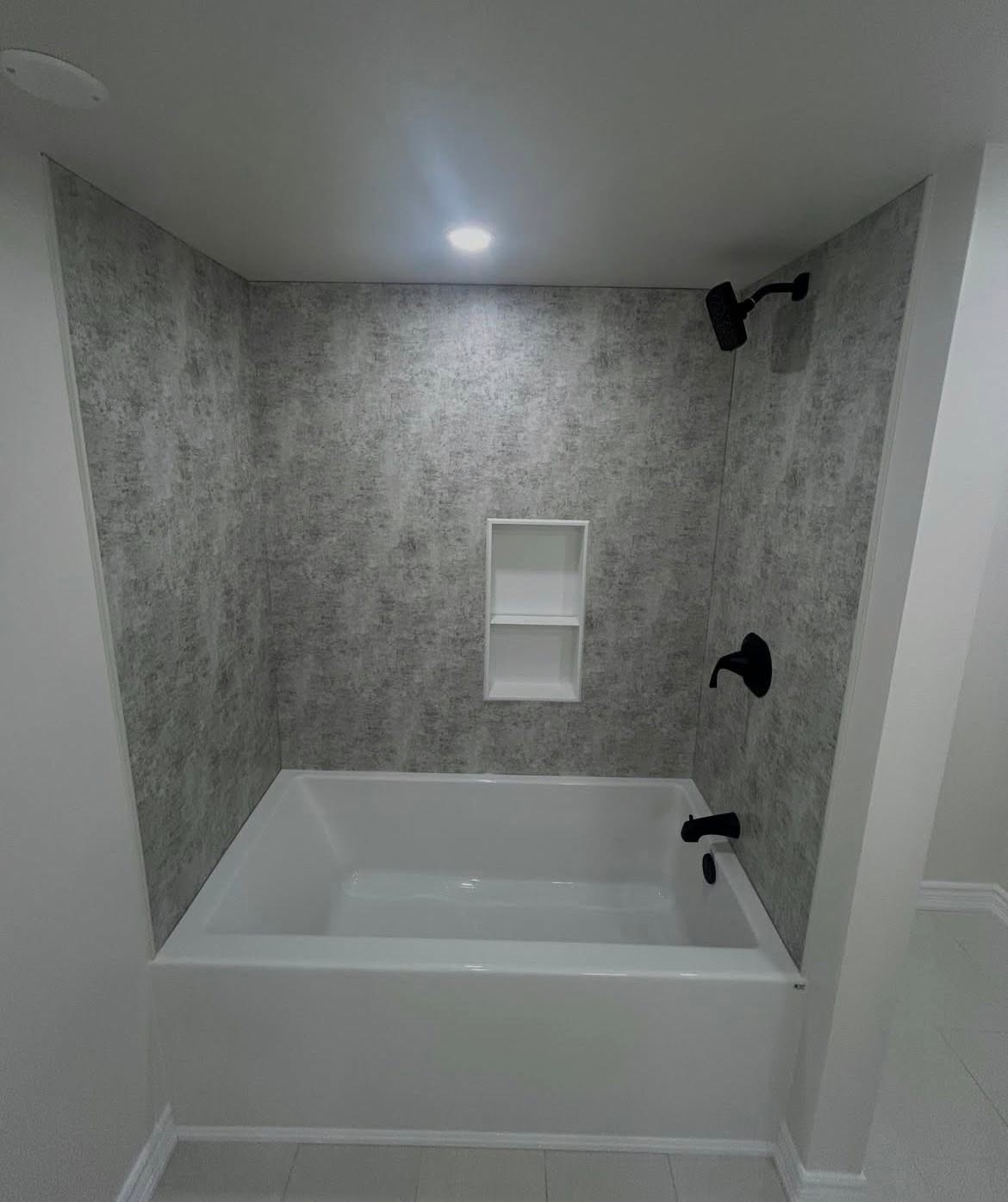 Patterned tub surround with a recessed shelf and dark fixtures.