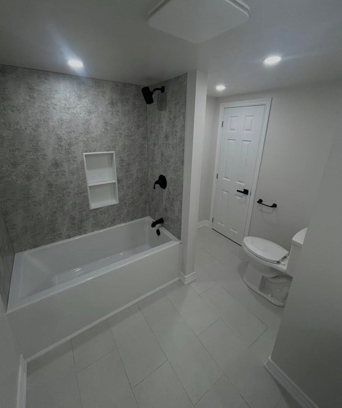 White bathtub with a patterned tile surround and recessed shelf.
