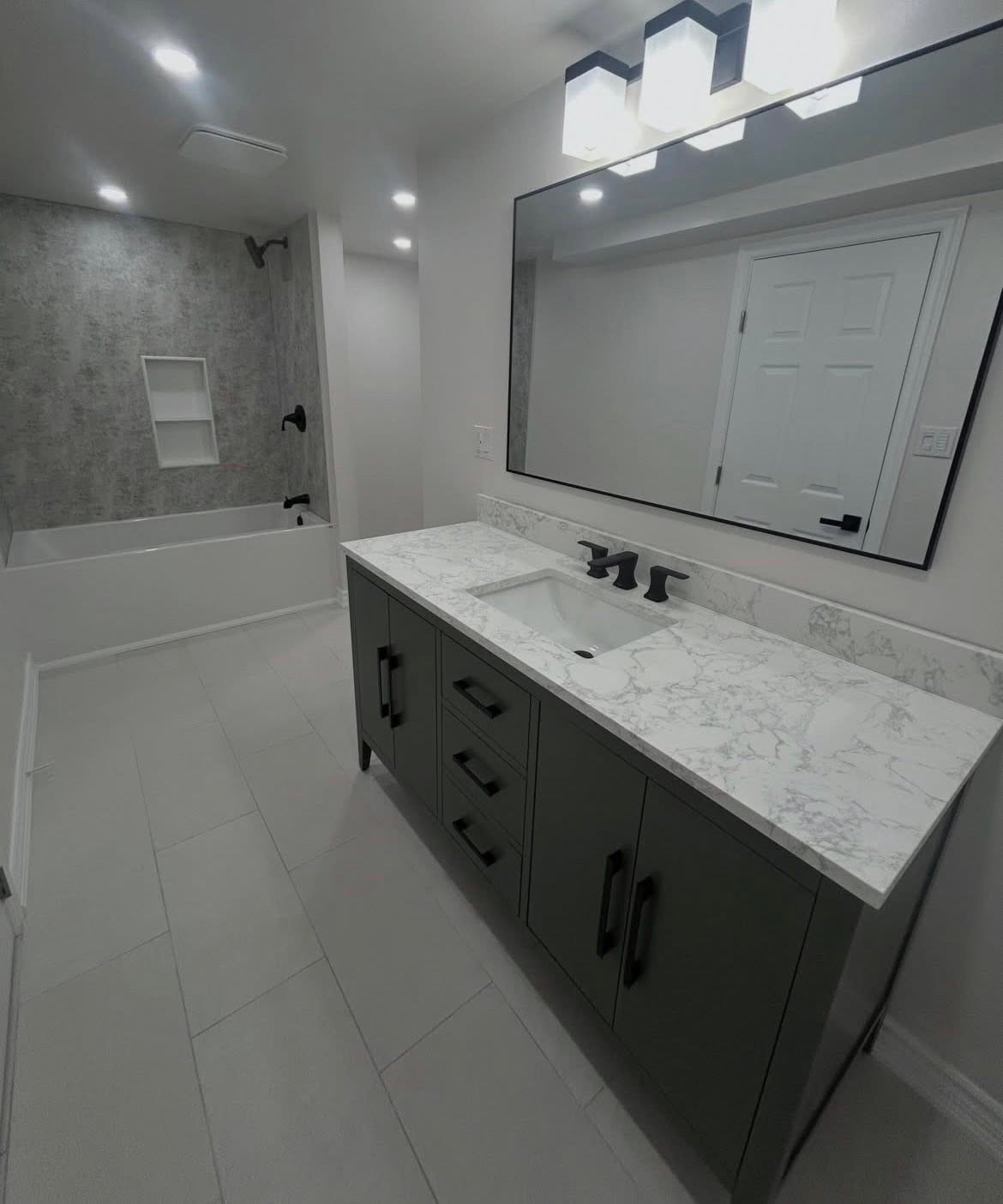 Dark vanity with a light countertop, framed mirror and overhead lighting.